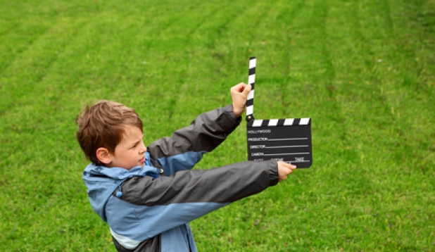 ein Kind steht auf einer Wiese und haelt eine Filmklappe